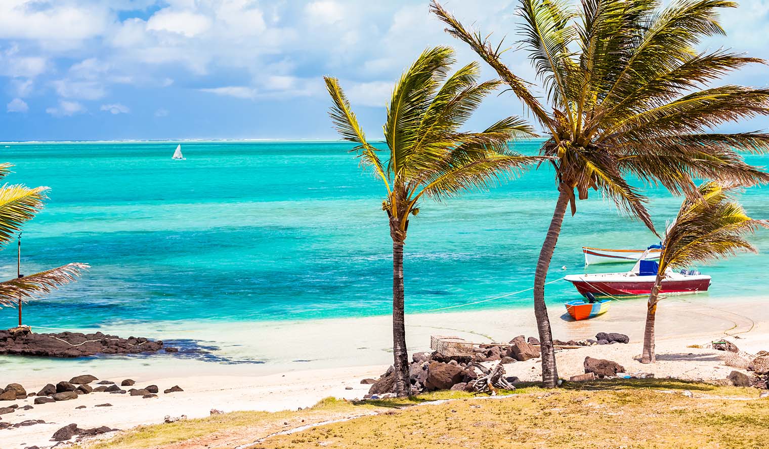 Traumhafter Strand auf Rodrigues, Mauritius mit türkisblauem Meer, Palmen, Fischerbooten und Segelboot in der Ferne – ideal für Mauritius Badeferien, Wassersport und Erholung
